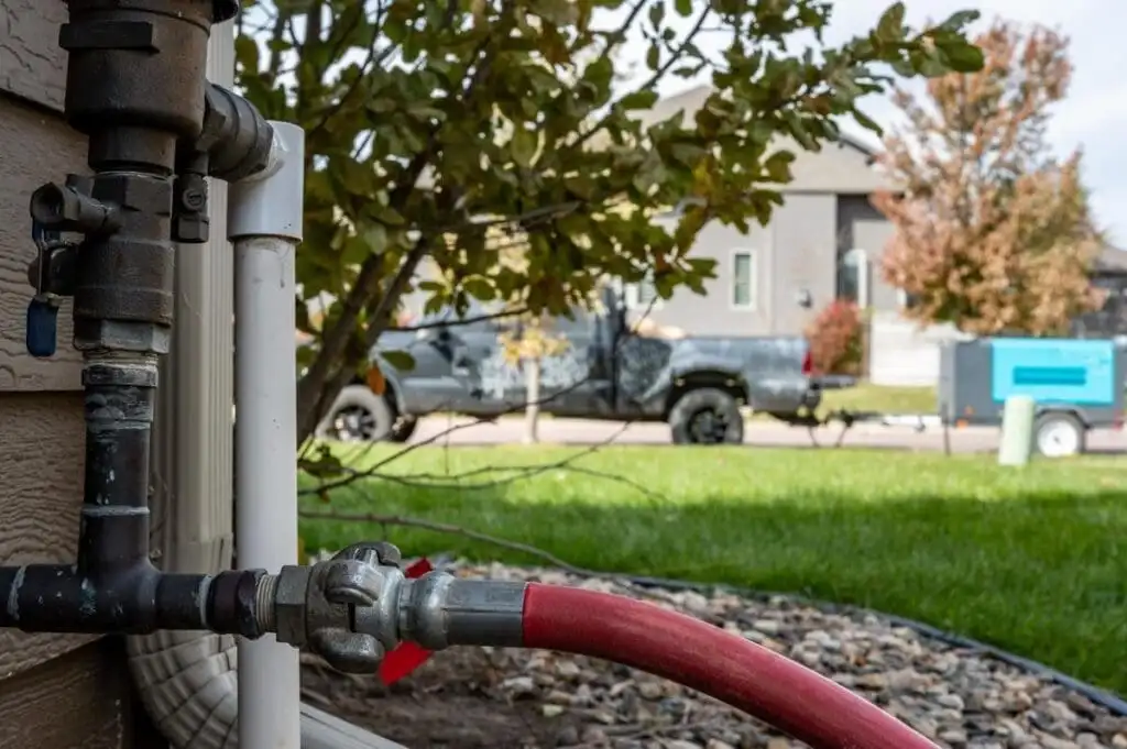 Residential irrigation backflow preventer and supply assembly during winterization with red hose connected to compressed air source