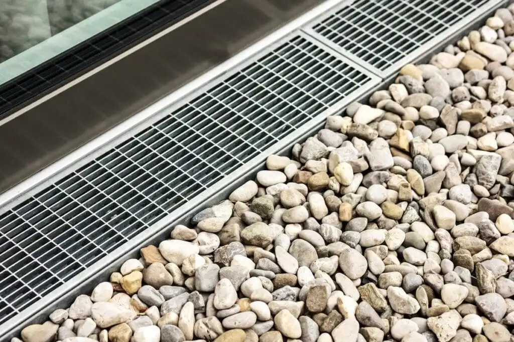 Channel drain with decorative grate and river rock — a surface drainage solution often confused with a French drain