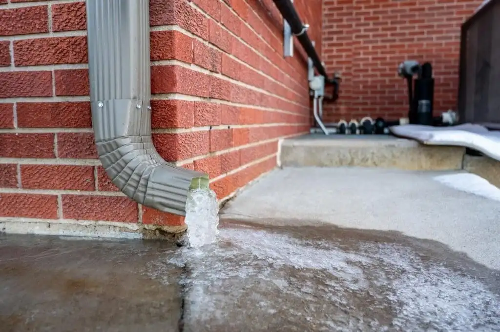Downspout discharging directly onto concrete with water running toward the foundation