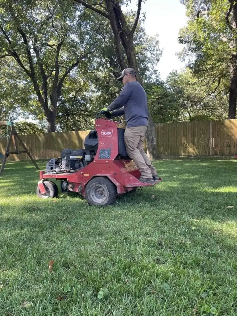Complete Lawn Care crew member operating a commercial Toro stand-on aerator in a Tulsa backyard