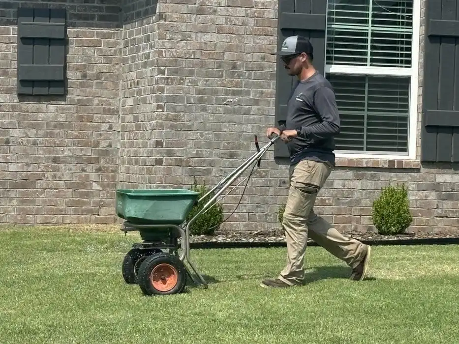 A Complete Lawn Care technician applies granular fertilizer to a Tulsa-area lawn