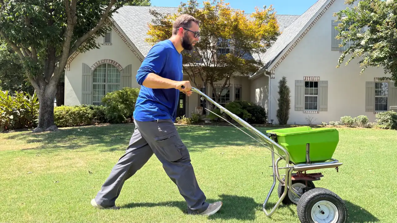 Complete Lawn Care technician pushing a broadcast spreader across a front lawn