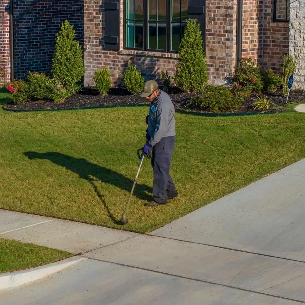 Complete Lawn Care technician trimming the lawn edge along a sidewalk